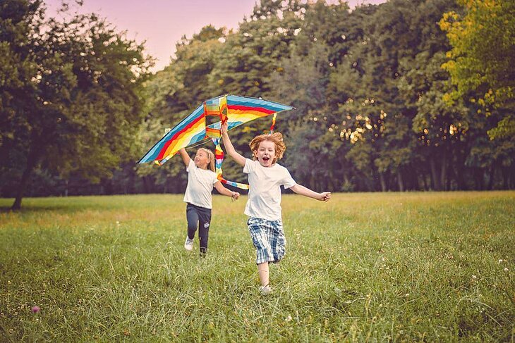 Children Flying a Kite During Summer Holidays Two children run through a field, flying a colourful kite under the summer sun.