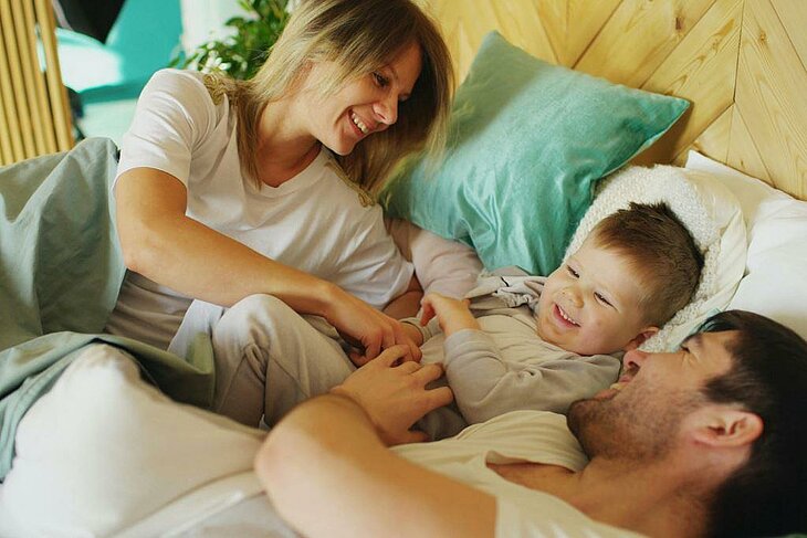 Relaxing Family Morning During the Holidays Parents and child smiling in bed, enjoying a peaceful and shared holiday moment.