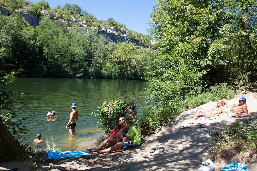 Families enjoying a swim and relaxing on a shaded riverside beach, near the Ardèche Gorges.
