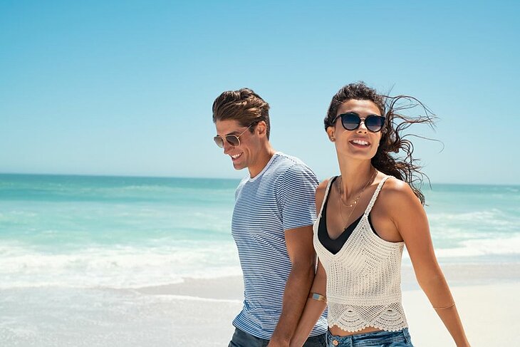 A couple walking hand in hand on a summer beach, blue sky and ocean, ideal for an outdoor getaway for two.