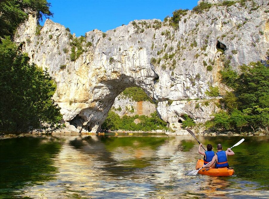 Canoeing under the Pont d’Arc, the iconic natural arch of the Ardèche Gorges, a region to explore during a holiday at a campsite.