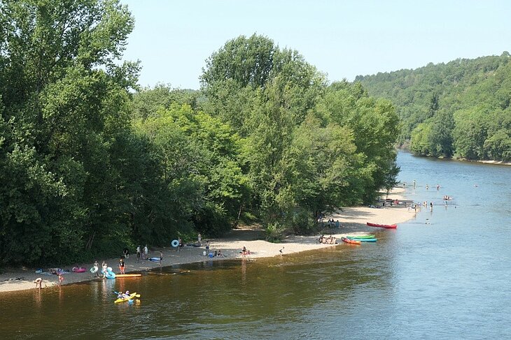 Canoes on the Vézère River Beach on the banks of the Vézère River near Le Bugue, with swimmers and canoes for an outdoor adventure in the Dordogne.