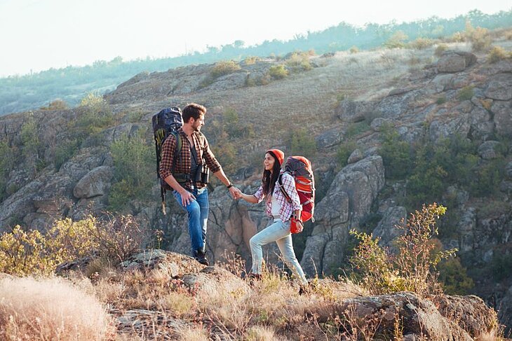 A couple hiking in the mountains, backpacks on and natural landscapes all around, sharing a moment of disconnection during a getaway for two.