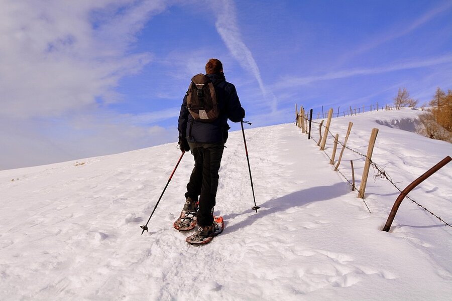 A snowshoer makes their way along a snowy trail under a clear blue sky, surrounded by untouched nature. Enjoy a winter holiday to remember with a stay at a winter-ready campsite with Sites et Paysages.
