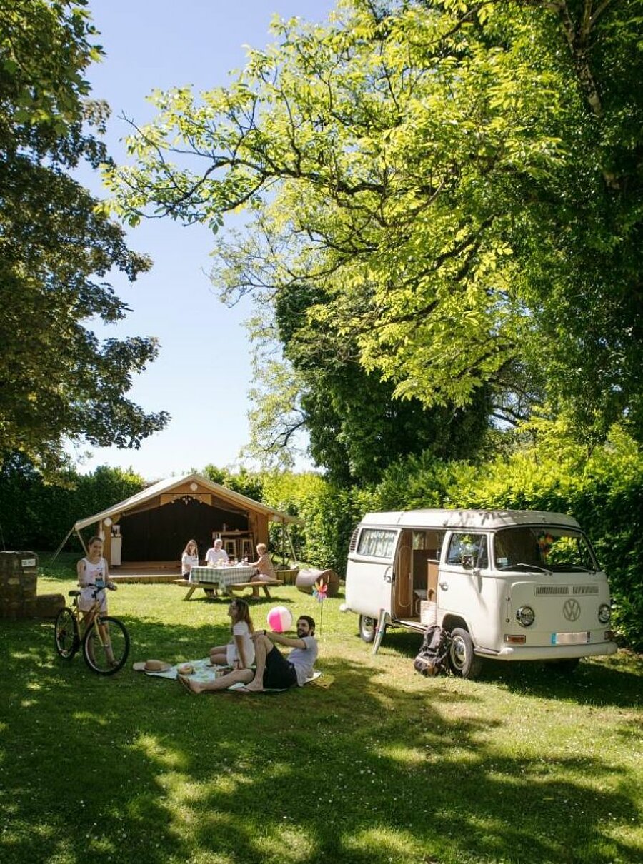 A family enjoying an Easter weekend camping with Sites et Paysages, between a converted van and a lodge tent, in a lush natural setting.