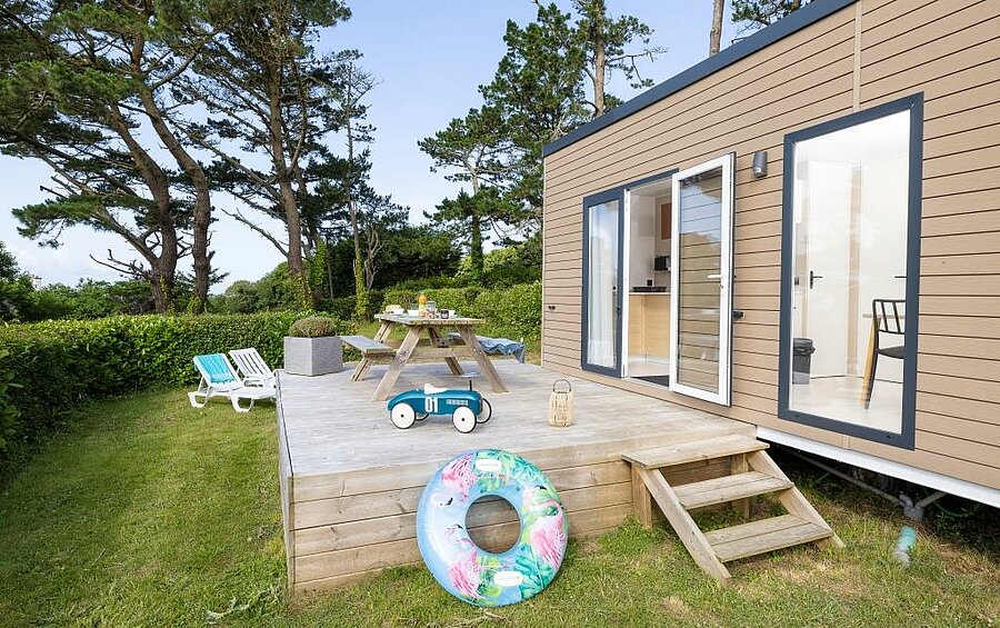 Mobile home with wooden terrace, sun loungers and outdoor dining area in a family-friendly campsite in Brittany