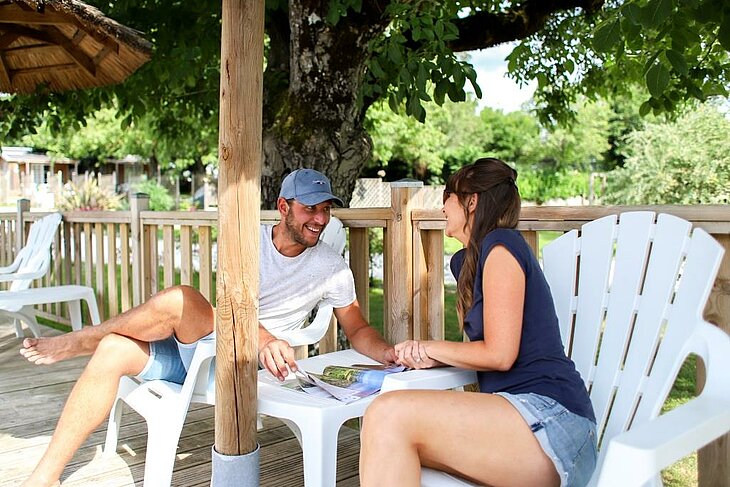 Smiling couple sitting on a shaded campsite terrace, relaxing moment illustrating early booking couple.