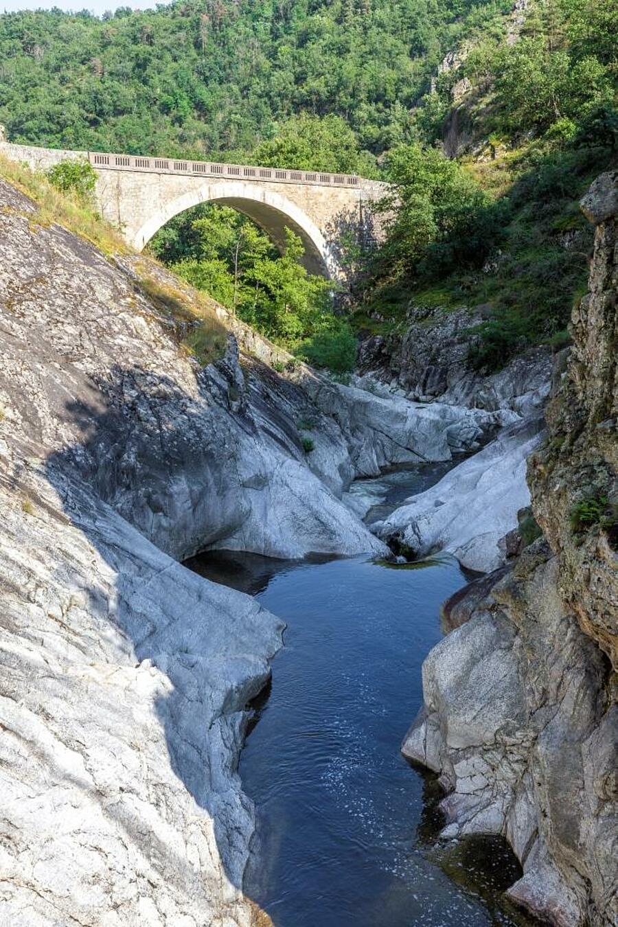 A picturesque bridge spanning the Ardèche Gorges, surrounded by rocky formations and lush nature — perfect for a camping holiday in Ardèche.