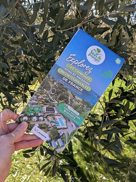Hand holding the 2026 Michelin road map of Sites et Paysages campsites, offered free to plan a nature road trip in France.