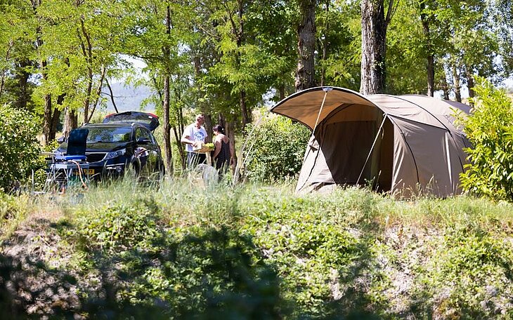 Couple setting up their tent under the trees, a peaceful and joyful Early Booking camping moment in nature.