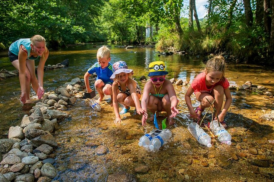 Children playing in a river with handmade boats in the heart of nature, a fun and friendly family activity during camping holidays in Auvergne-Rhône-Alpes.