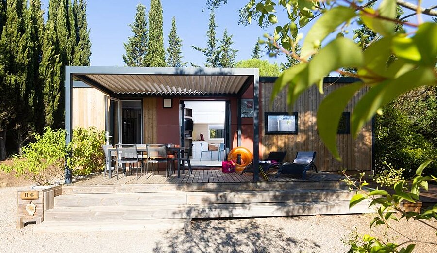 Modern mobile home with shaded terrace, table and sunbeds, nestled in greenery near Carcassonne.