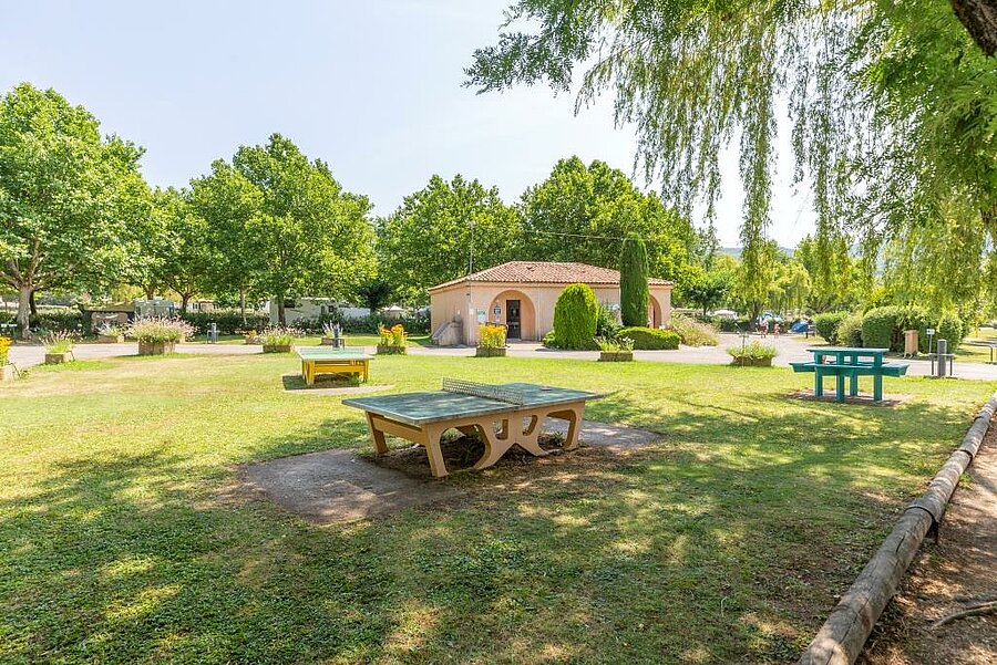 Shaded communal areas of a campsite near Forcalquier, leisure tables and green surroundings for friendly holidays in Provence.