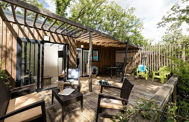 A wooden terrace with partial shade outside campsite accommodation surrounded by trees.