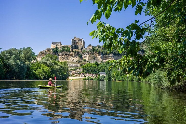 Canoeing on the Dordogne with a hilltop castle in the background, an ideal outdoor activity for exploring the valley in the open air.