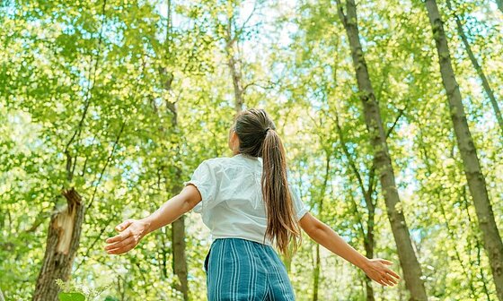 Young girl with arms wide open in the forest, a symbol of reconnecting with nature and sustainable tourism with Sites et Paysages.