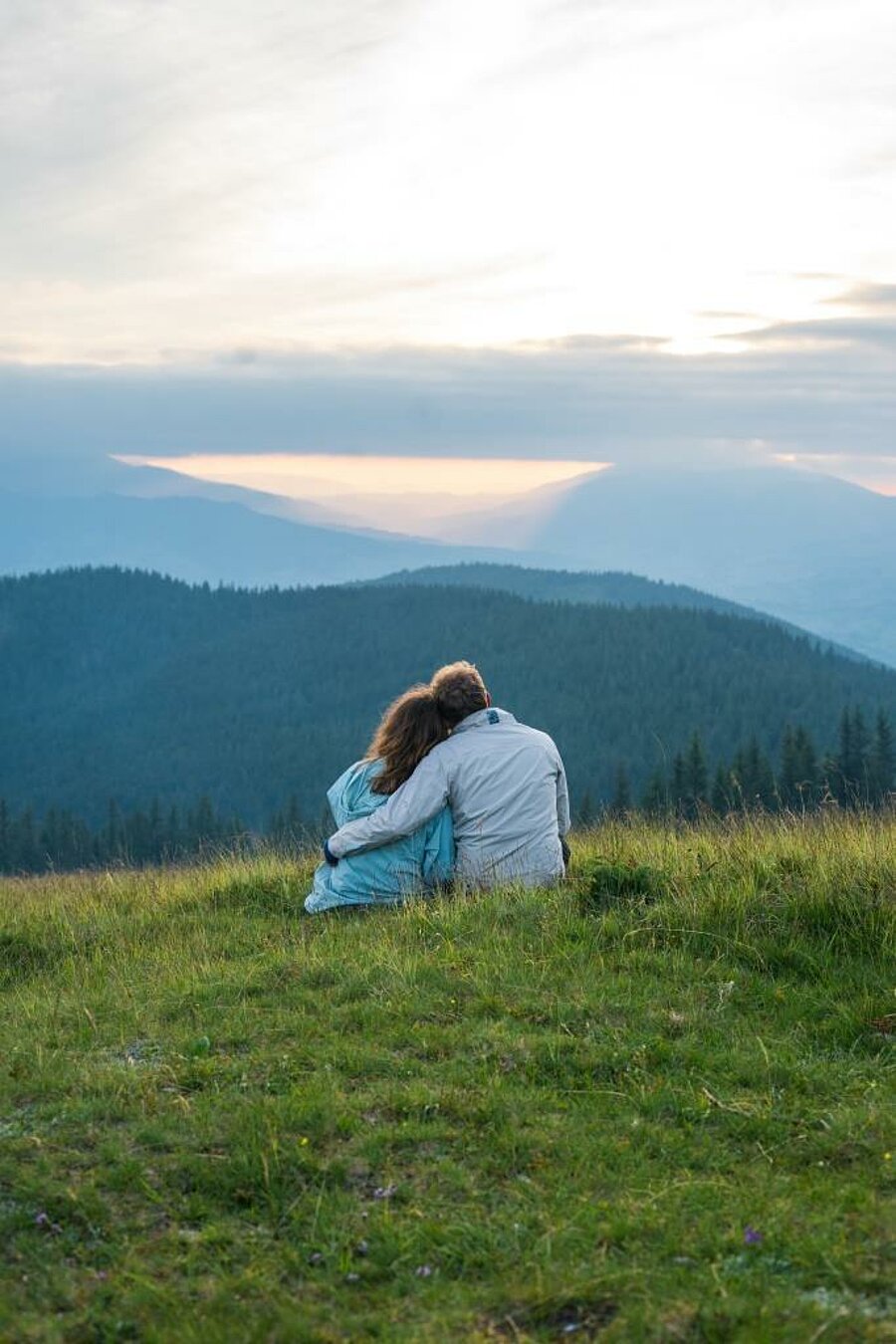 Couple sitting together in the grass facing mountain views at sunset, peaceful setting for a romantic camping weekend for two.