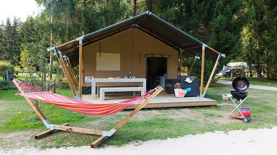Equipped tent with terrace and hammock in a flowery setting, perfect for a peaceful nature getaway.