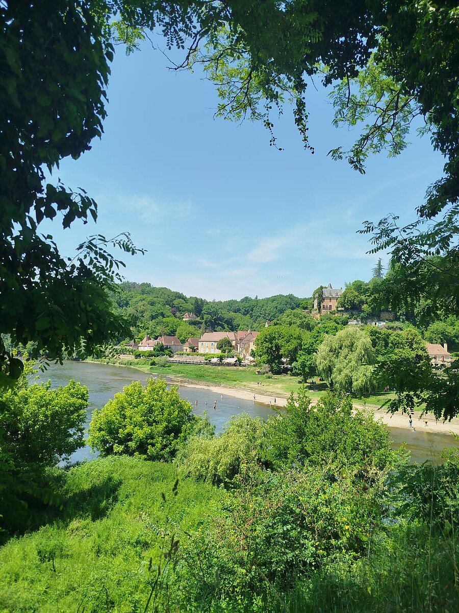 View of a picturesque Dordogne village with the river and a natural beach, close to campsites for exploring the region.