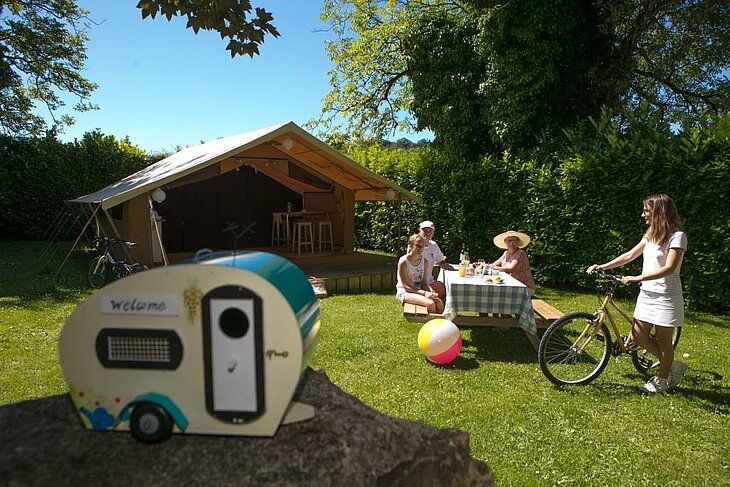 A family in front of a lodge tent at a Sites et Paysages nature campsite, with bicycles and an outdoor meal.