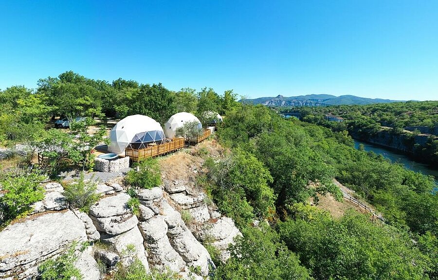 Wooden terrace with private jacuzzi and sun loungers at a campsite near Balazuc, overlooking the Ardèche gorges and forest.