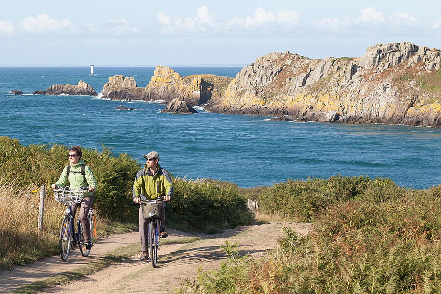 A couple cycling and enjoying the natural scenery near the campsite in Cancale, Brittany, with a view of the Pointe du Grouin.
