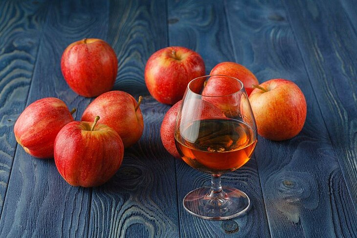 A glass of Calvados and red apples on a wooden table, symbol of the Pays d’Auge distilleries in Normandy to visit with friends.
