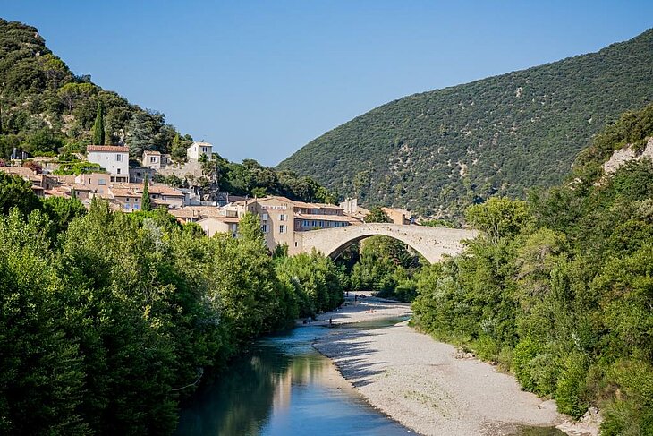 Romanesque bridge in Nyons spanning the Eygues River, with houses in the old town and the hills of Drôme Provençale.