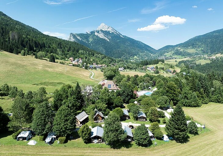 Aerial view of a nature campsite nestled in the mountains, symbolizing human-scale and peaceful holidays in the Alps.