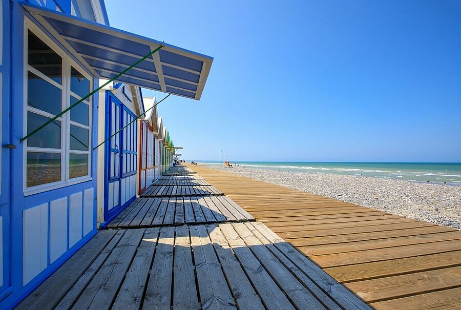 Colourful beach huts and wooden boardwalk in Cayeux-sur-Mer by the sea, an iconic coastal landscape of the Baie de Somme.