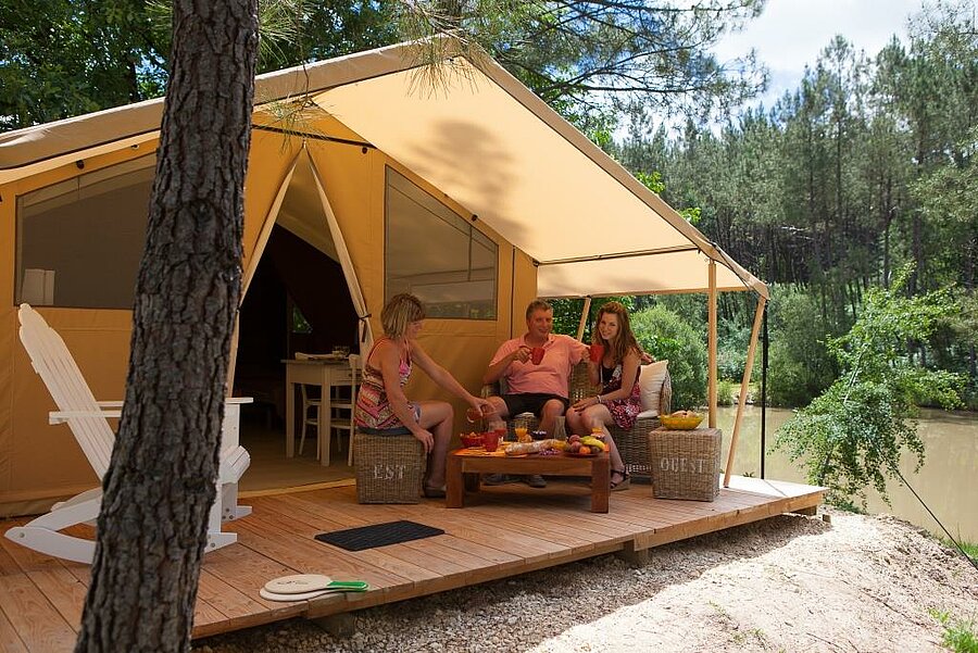 Family relaxing on the terrace of a lodge tent in a campsite near Saint-Émilion, a comfortable and natural Camping Saint-Émilion rental.