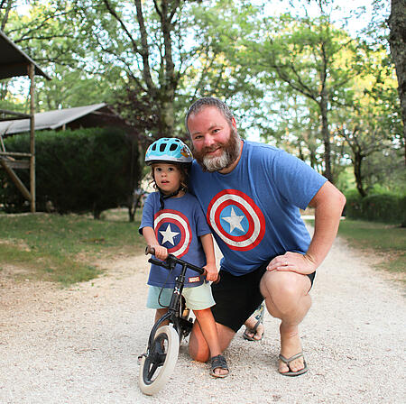 A father and son wearing matching T-shirts pose in front of their eco-friendly accommodation, symbolizing concrete tools to act and raise awareness about sustainable tourism.