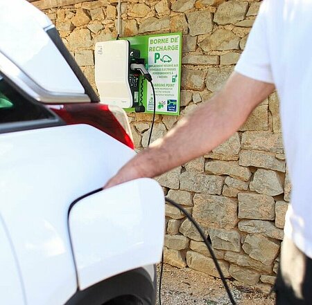 Charging an electric car at a charging point installed on a campsite, with a stone wall in the background.