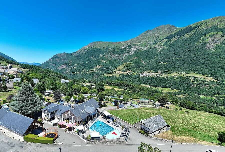 Aerial view of Pyrénévasion campsite near Lourdes, featuring a heated pool and stunning green mountain backdrop.