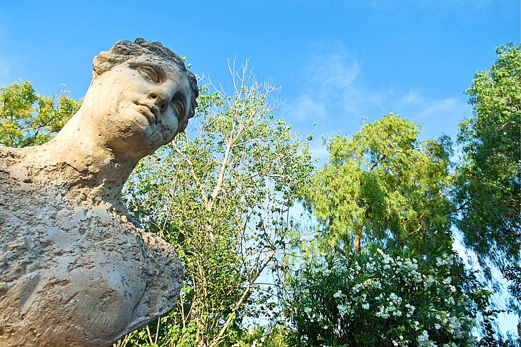 Ancient sculpture of a woman with a tilted gaze, surrounded by greenery and blue skies in Martres-Tolosane
