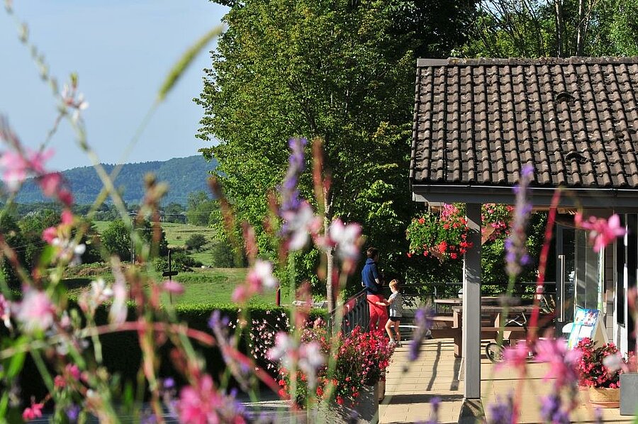 Family standing on the flower-filled terrace of a campsite rental with nature views in Bourgogne-Franche-Comté, France.