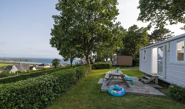 Terrace of a mobile home with picnic table, greenery, and bay views in Telgruc-sur-Mer.