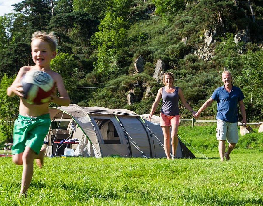 Family with child playing in front of a tent at an ACSI campsite, nature stay on a spacious and affordable pitch.