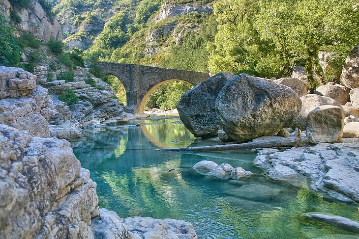 Natural landscape of the Méouge Gorges near Sisteron, with its historic stone bridge and turquoise waters — an ideal spot for outdoor activities like hiking and swimming.