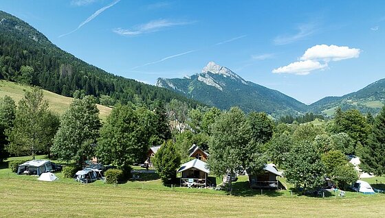 [Translate to Anglais:] Vue d’un camping à taille humaine niché au cœur des montagnes, entouré de nature préservée et d’hébergements confortables, idéal pour des vacances en famille.