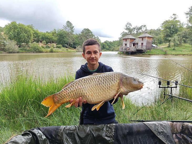 Young angler holding a carp at Domaine de l’Étang de Bazange in Monfaucon, a nature activity for all ages in Dordogne.