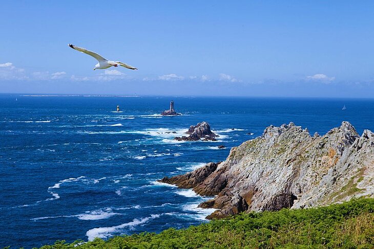 Steep cliffs of the Pointe du Raz in Brittany, rough sea and offshore lighthouse, a spectacular natural site to enjoy when wondering what to do in Brittany.