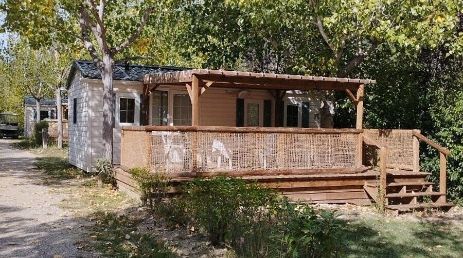 Mobile home with a covered wooden terrace and outdoor furniture, surrounded by trees at Domaine de l’Écluse near Mont Ventoux.