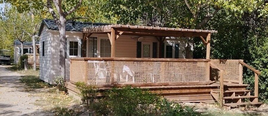 Mobile home with a covered wooden terrace and outdoor furniture, surrounded by trees at Domaine de l’Écluse near Nyons.