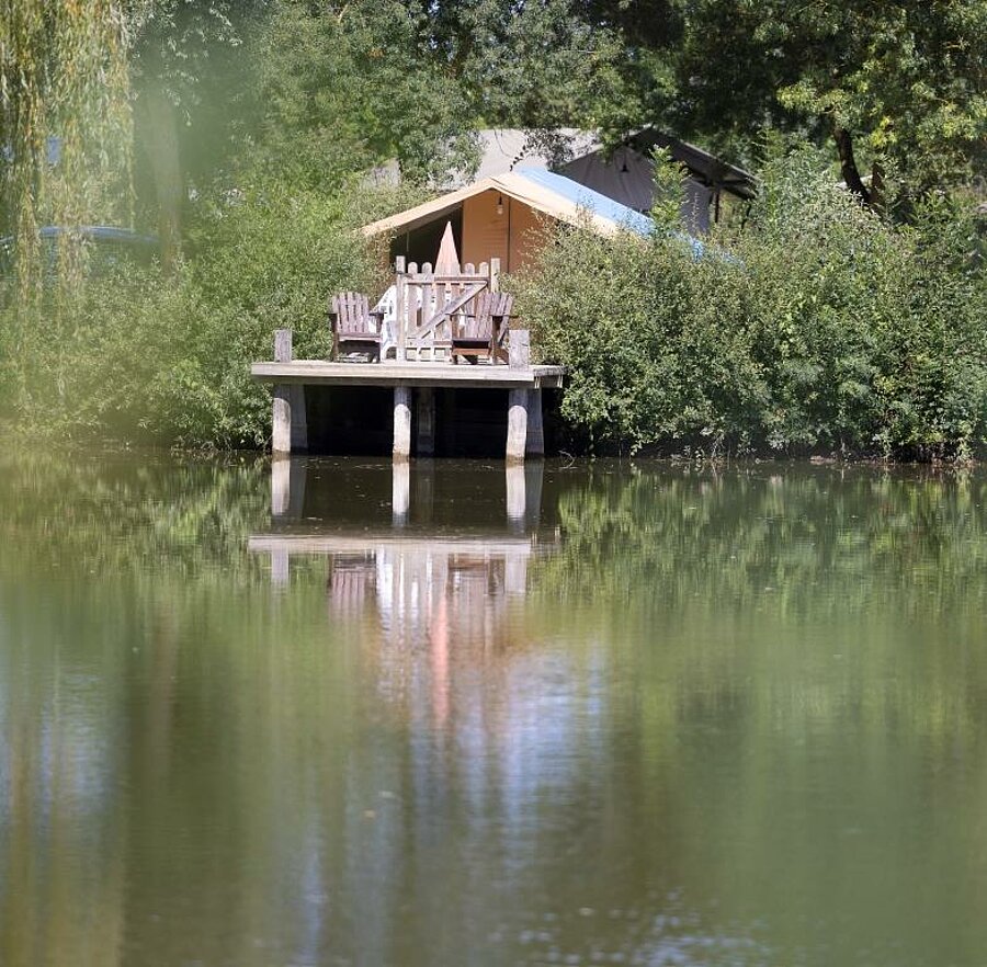 Comfortable lodge tent with wooden deck overlooking a pond, nestled in nature – perfect for an unusual stay near the Châteaux de la Loire.