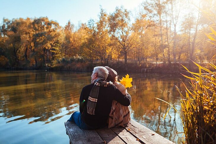 Enjoy a short autumn break for two Couple sitting by a lake, enjoying a peaceful moment in the autumn sunshine.