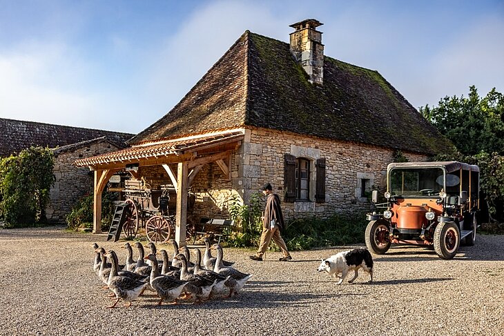 Village du Bournat © Déclic&Décolle Scene at Le Village du Bournat featuring a stone house, geese, a dog, a vintage vehicle and a person in period costume.