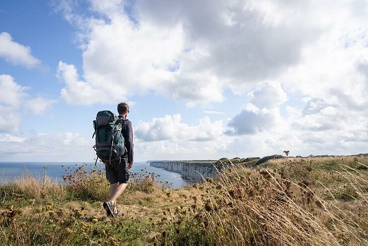 Hiker with backpack on the Normandy coastal cliffs facing the sea, a nature walk idea for solo travellers in Normandy.