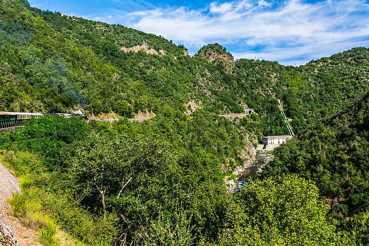 Ardèche Train winding along the mountainside through lush scenery near Tournon-Saint-Jean, a must-do experience around Eclassan for nature and railway heritage enthusiasts.