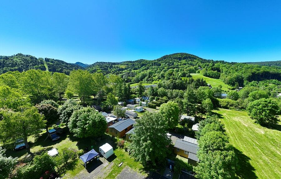Aerial view of Camping La Marmotte near Besse-et-Saint-Anastaise, green pitches and rentals surrounded by nature.